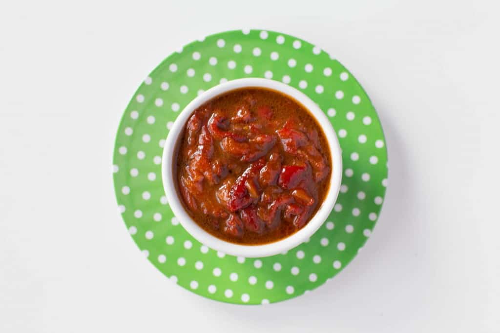 top down photo of Syrian Roasted Red Pepper salad with Pomegranate Molasses. The salad is bright red and is in a white bowl on top of a green and white polka dotted plate.