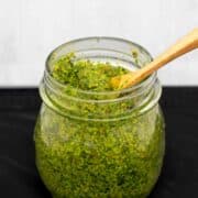 Single jar of bright green pesto with a wooden spoon sticking out.