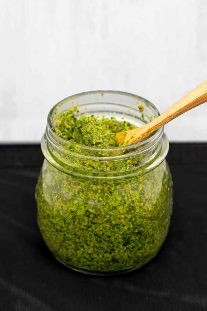 Single jar of bright green vegan wild garlic pesto with a wooden spoon sticking out.