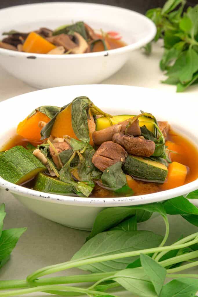 two bowls of soup surrounded by lemon basil. The backmost bowl is slightly out of focus.