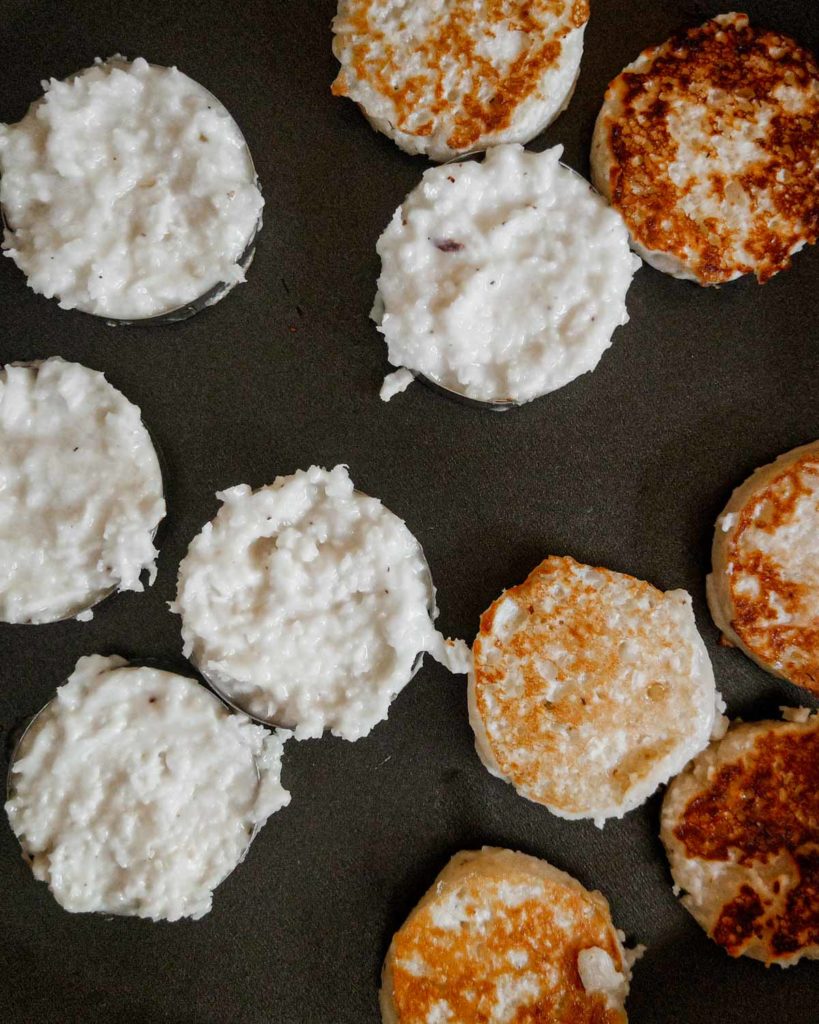 Kanom baa bin pancakes being fried, some with rings and others freeform