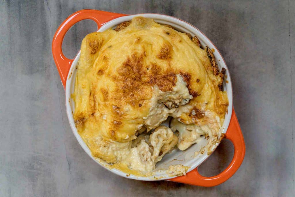 top down look at orange ovenproof dish with vegan cheesy cauliflower casserole, with a spoonful taken out