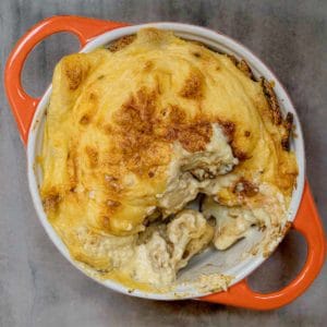 top down look at orange ovenproof dish with vegan cheesy cauliflower casserole, with a spoonful taken out