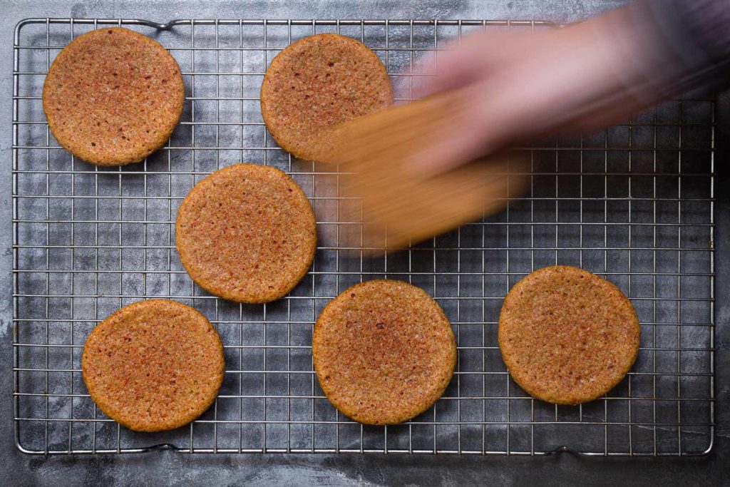 Turmeric cookies on a cooling rack, with a dark grey background. A blurred hand is taking two cookies.