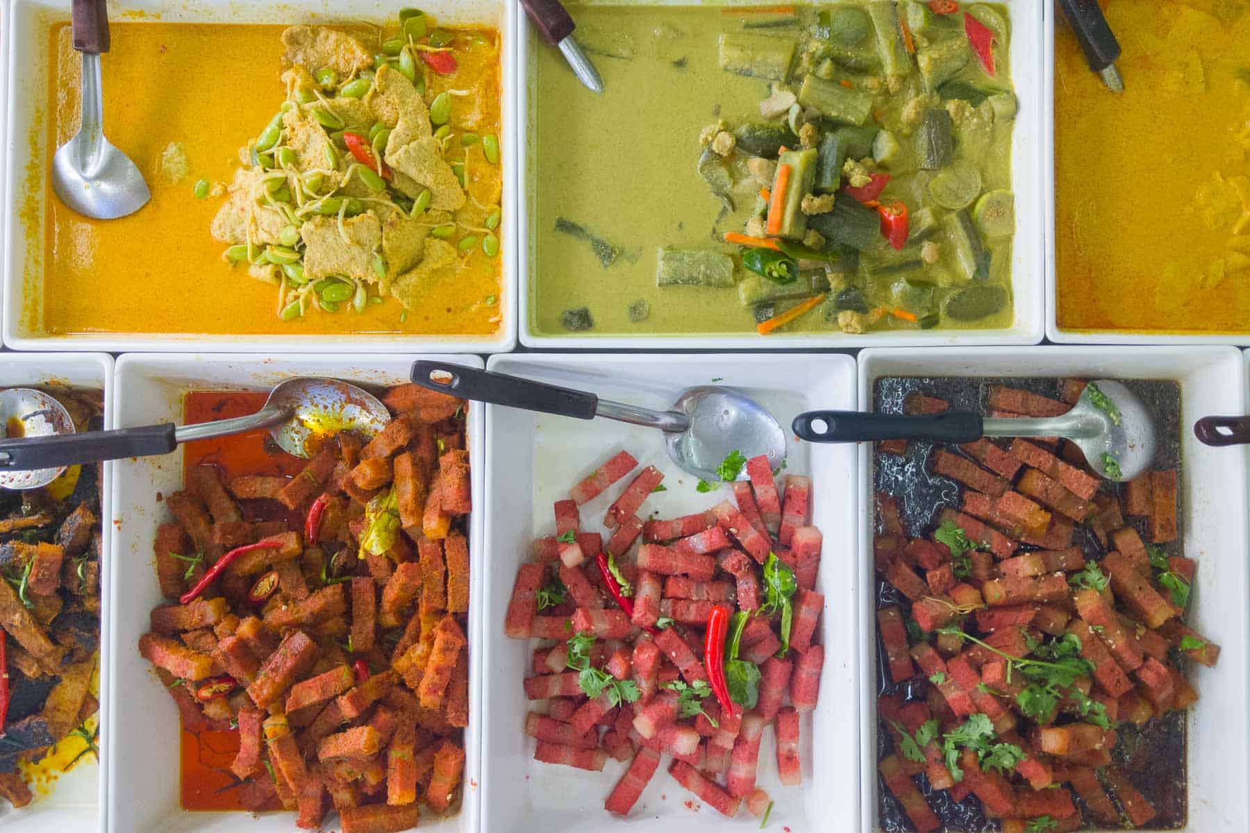 Shot from above of various foods for sale, including curries and vegan pork belly dishes