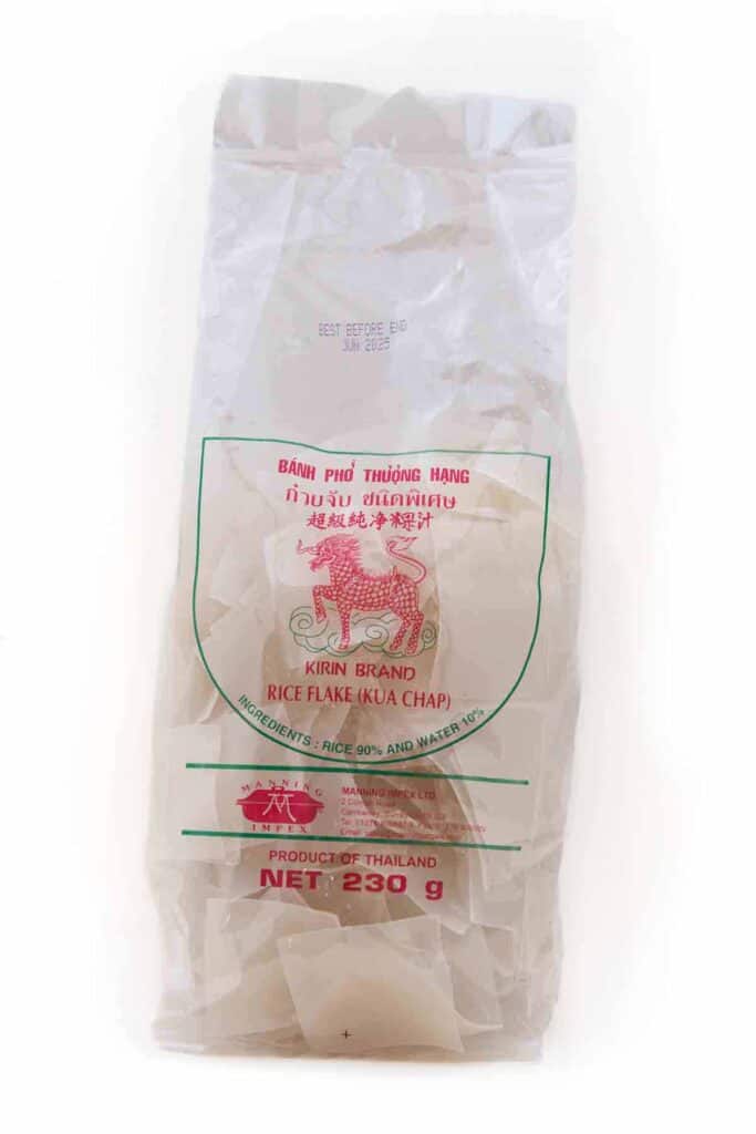 Plastic bag of flat rice flake noodles on a white background